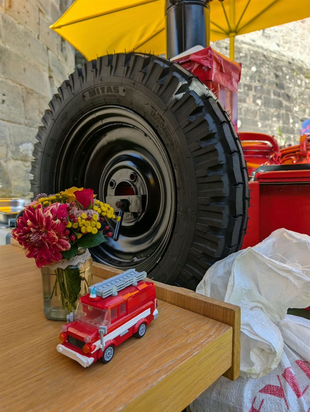 Blumenstrauß und Modellauto auf dem Stehtisch vor dem Rad der Gulaschkanone