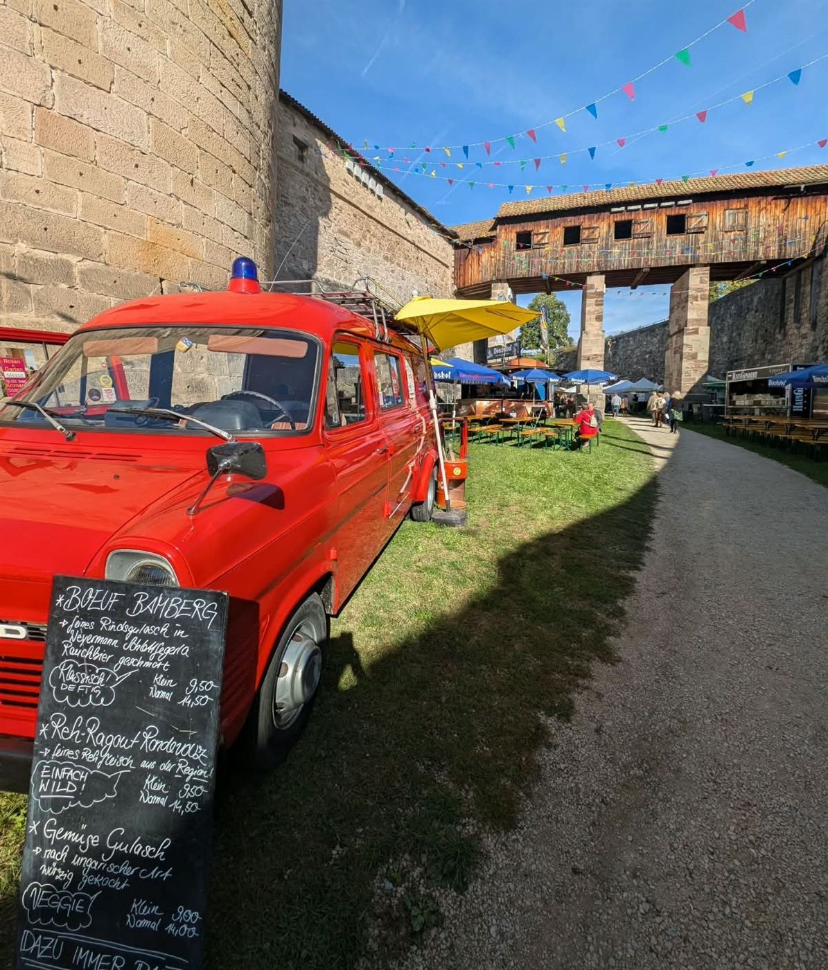 Roter Ford Transit Oldtimer mit Tafelmenü vor historischer Burgmauer